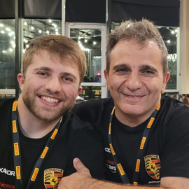 Zia Shlaimoun sitting with his son at a restaurant, both wearing black Porsche shirts and lanyards